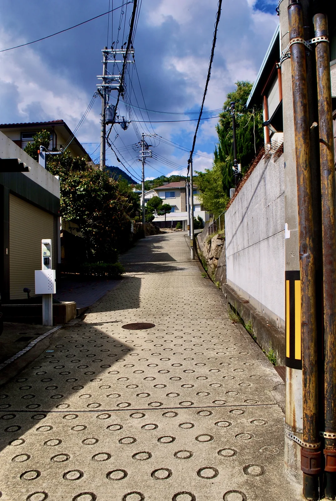 丸い滑り止めの坂の脇に、古い排水管と電柱が立つ風景