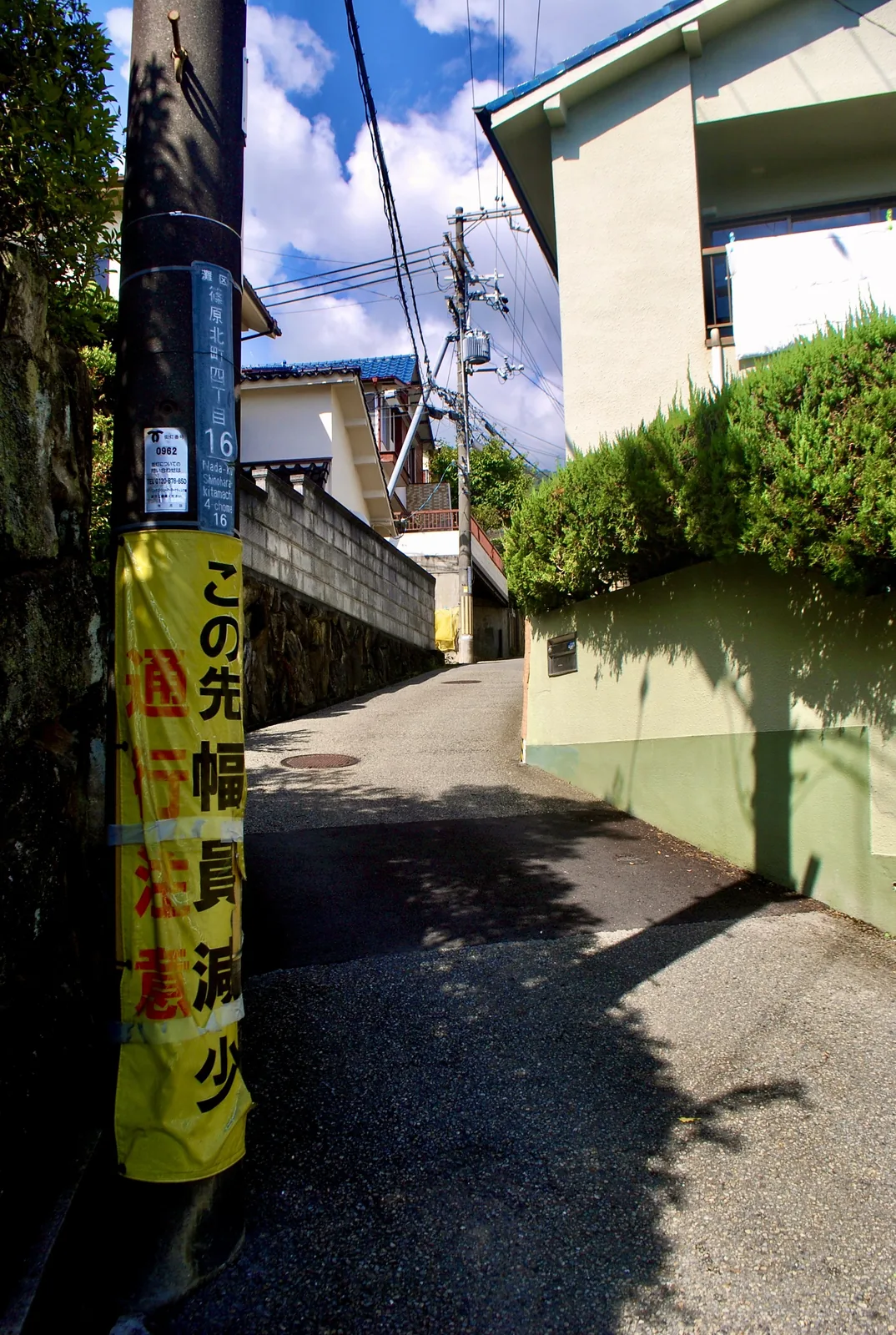 町名表示のある電柱の脇から、木陰の中を上っていく細い坂道