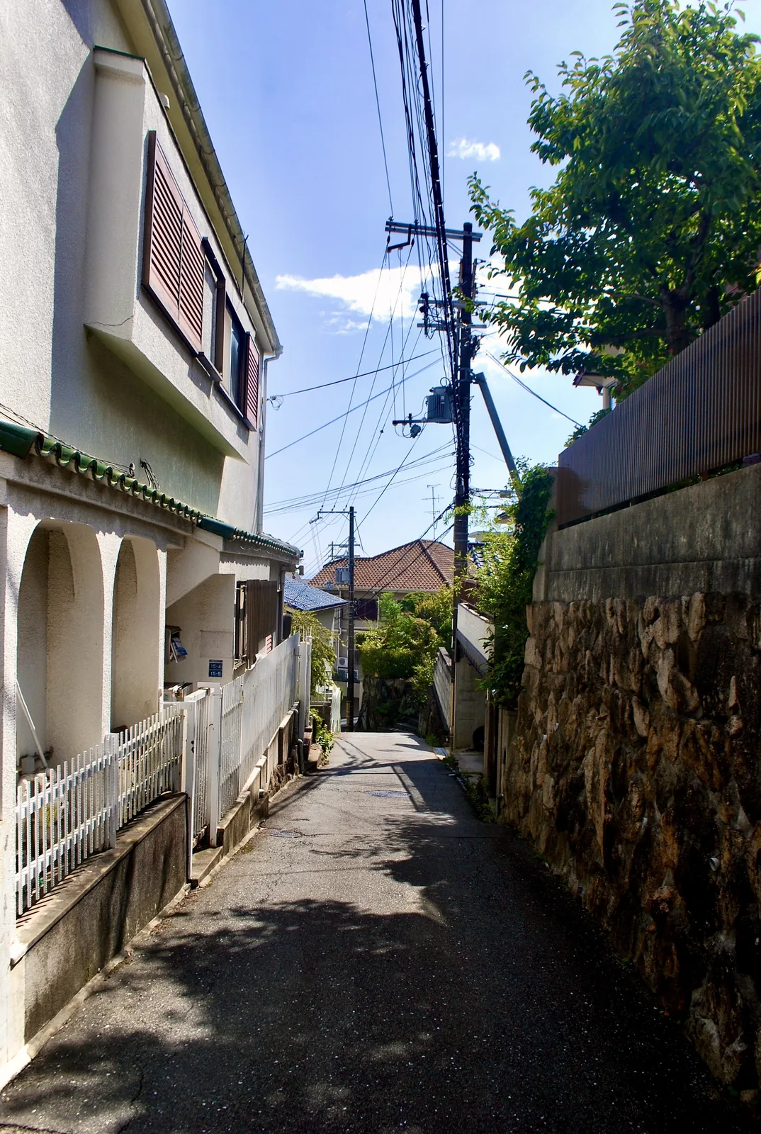 アーチのある家と石垣のあいだを、木陰の奥へ続く路地