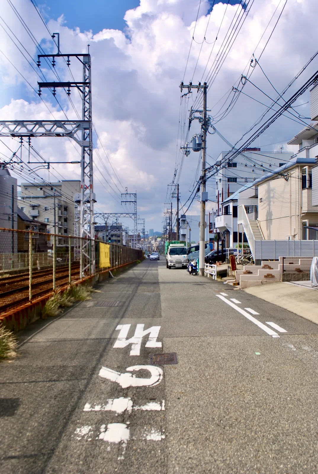 鉄塔と線路に沿って、雲の浮かぶ空の下をまっすぐ続く道