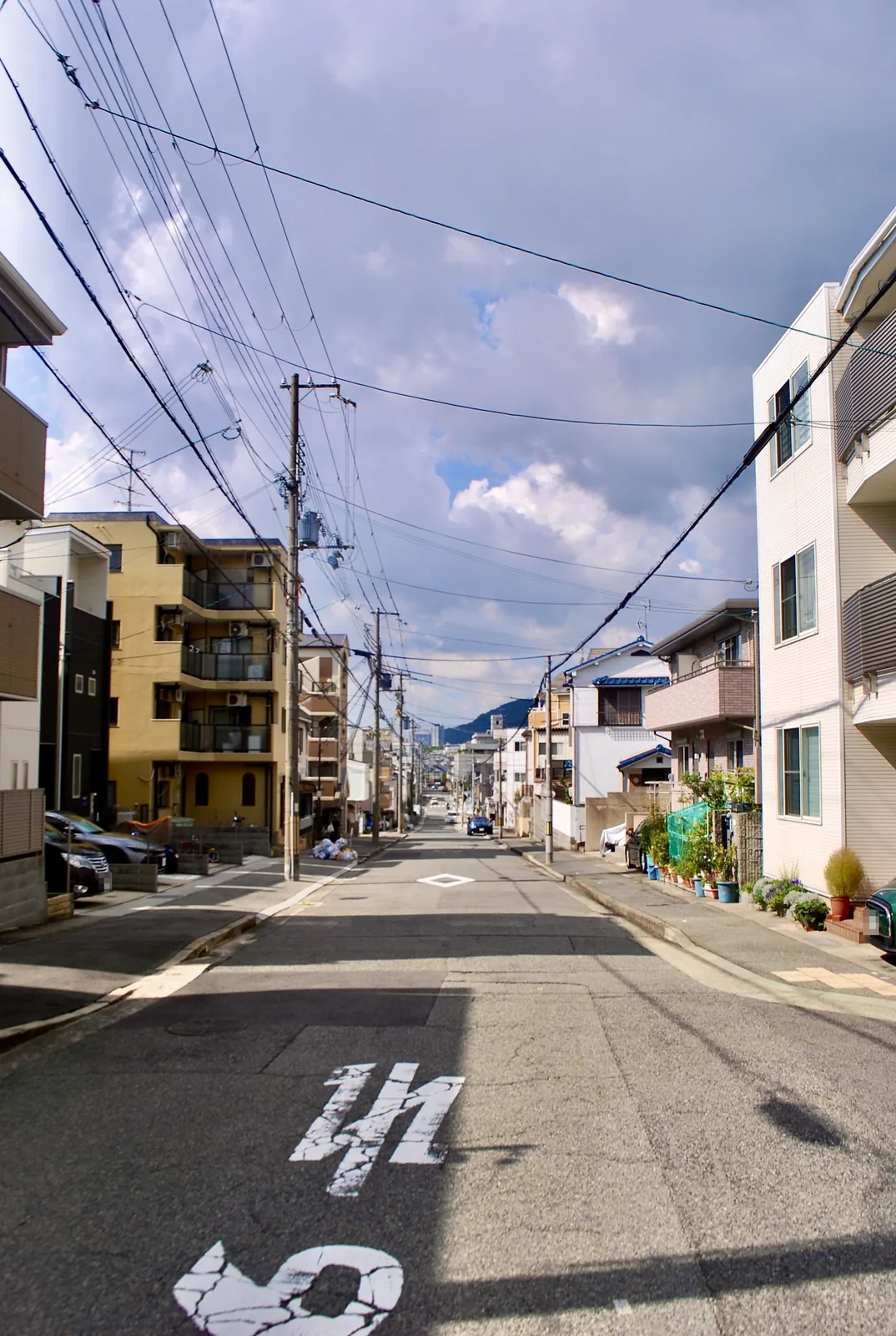 電線の張られた空の下、奥に山の見える住宅街の通り