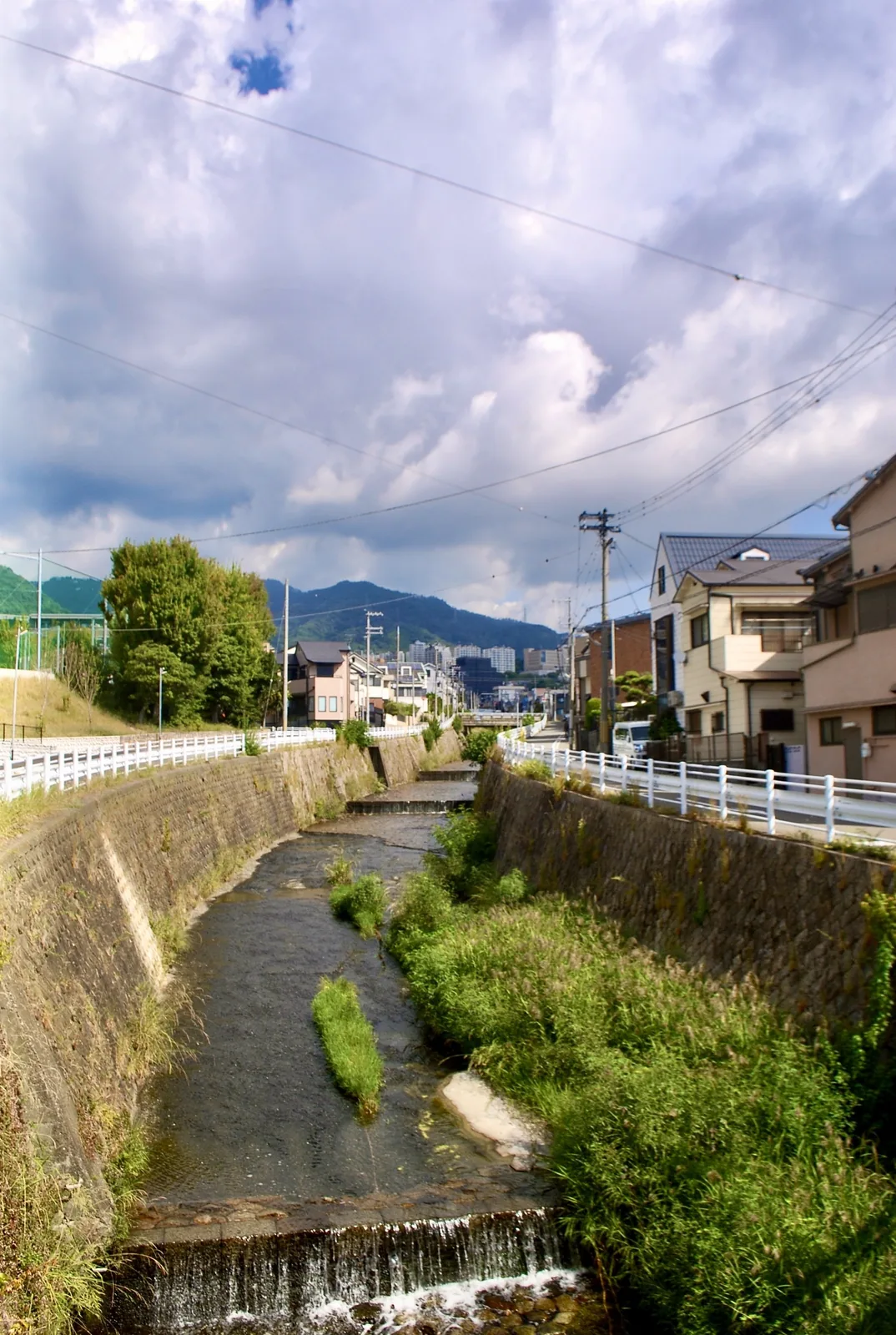 石積みの護岸のあいだを流れる川と、その奥に連なる山並み