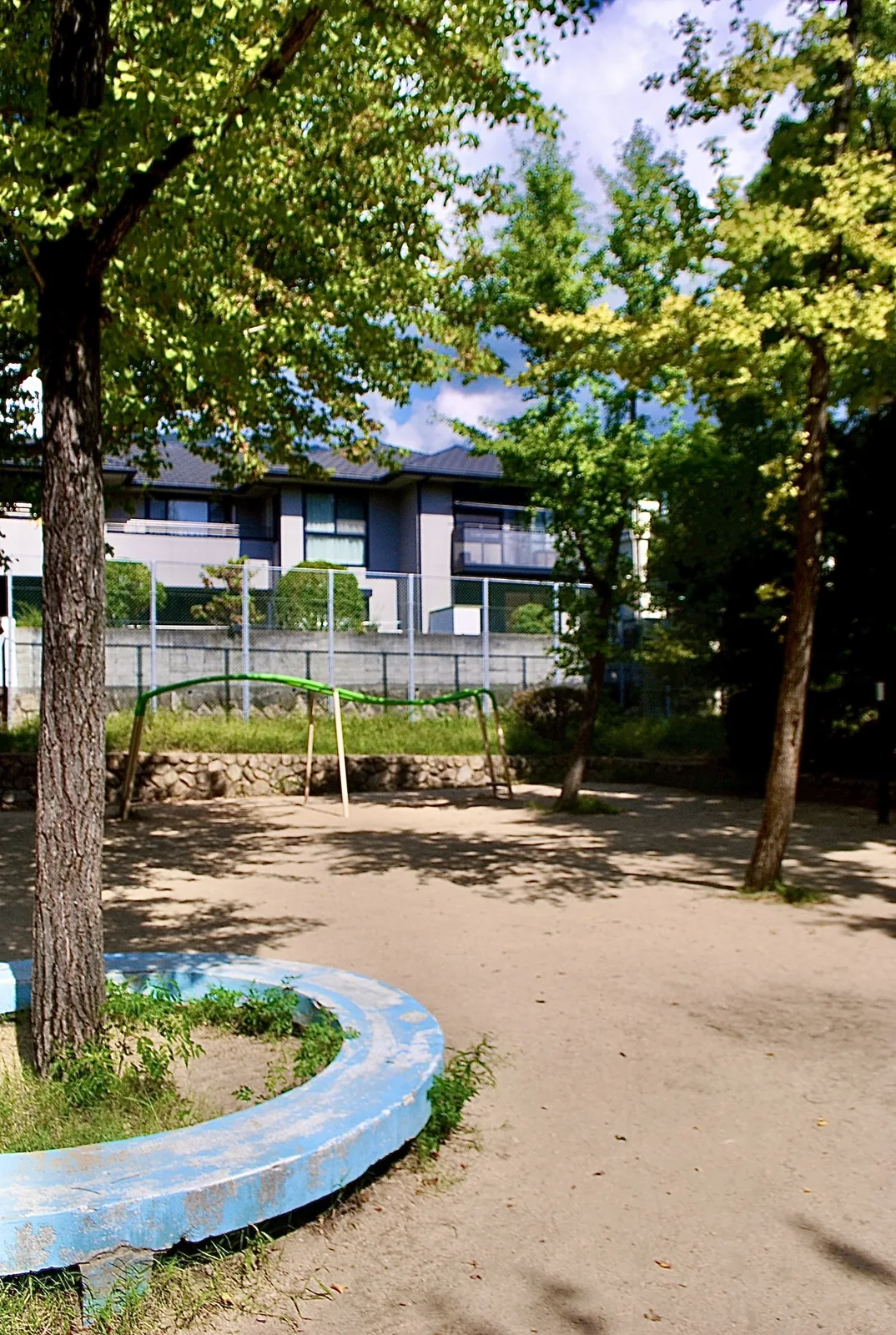 大きな木の下に、丸いベンチと遊具のある公園