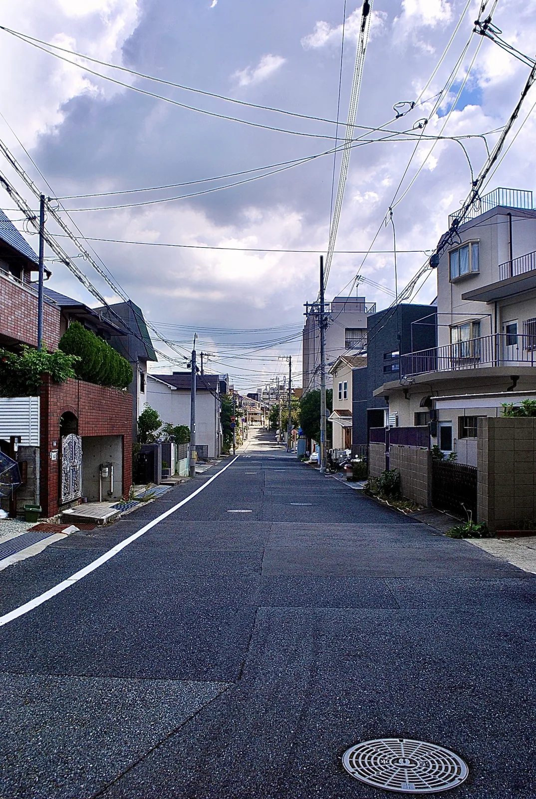雲の多い空に電線が広がる、住宅の並ぶ通り