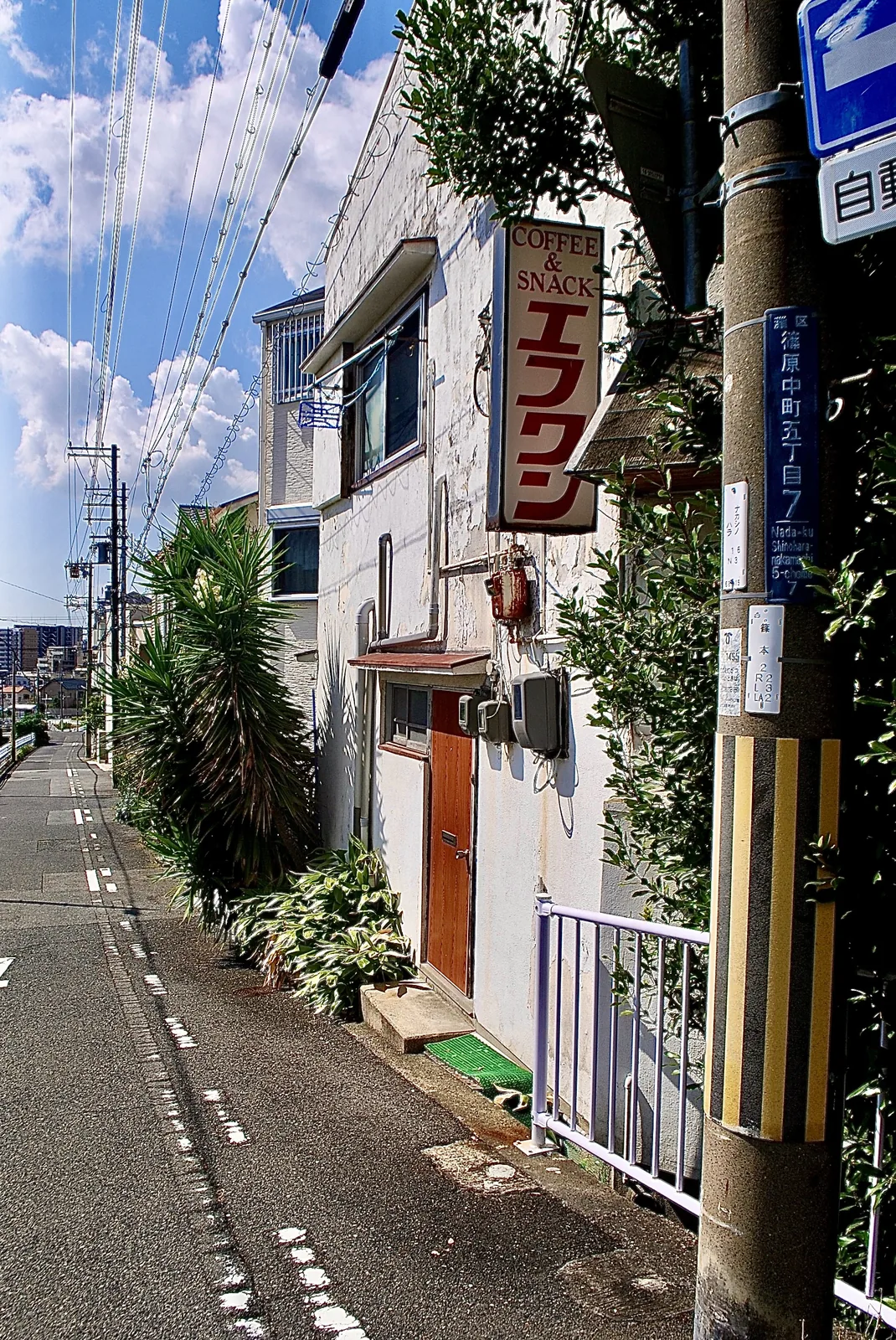 縦長の看板と赤い扉のある、白い外壁の店先