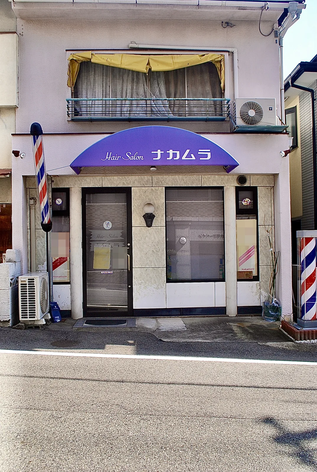 紫色の日よけと、二本のサインポールのある理容店の店先