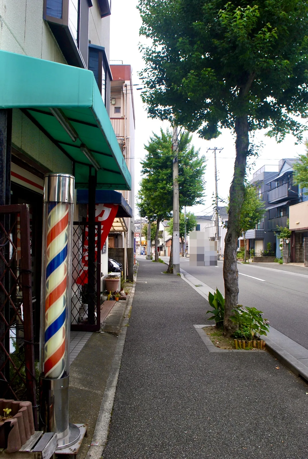 赤白青のサインポールの理容店から、並木の続く大通りの歩道