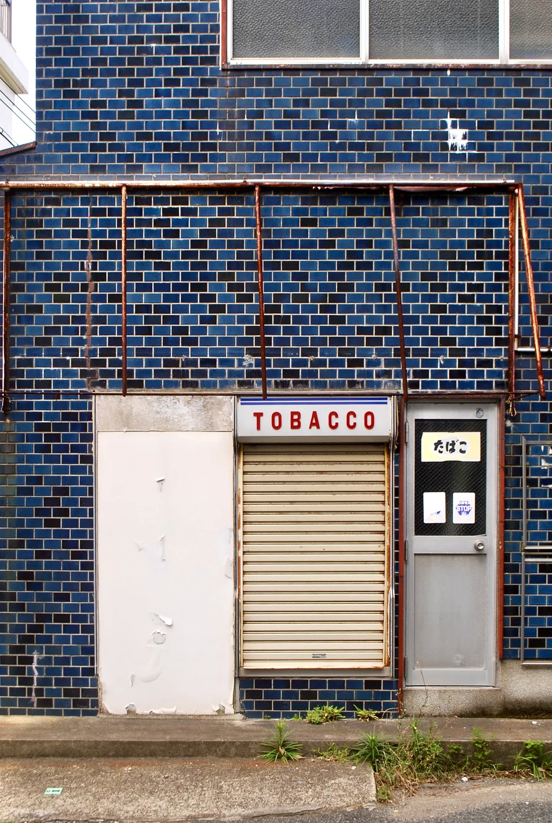 青いタイルの壁と「TOBACCO」の看板が残る、古いたばこ屋