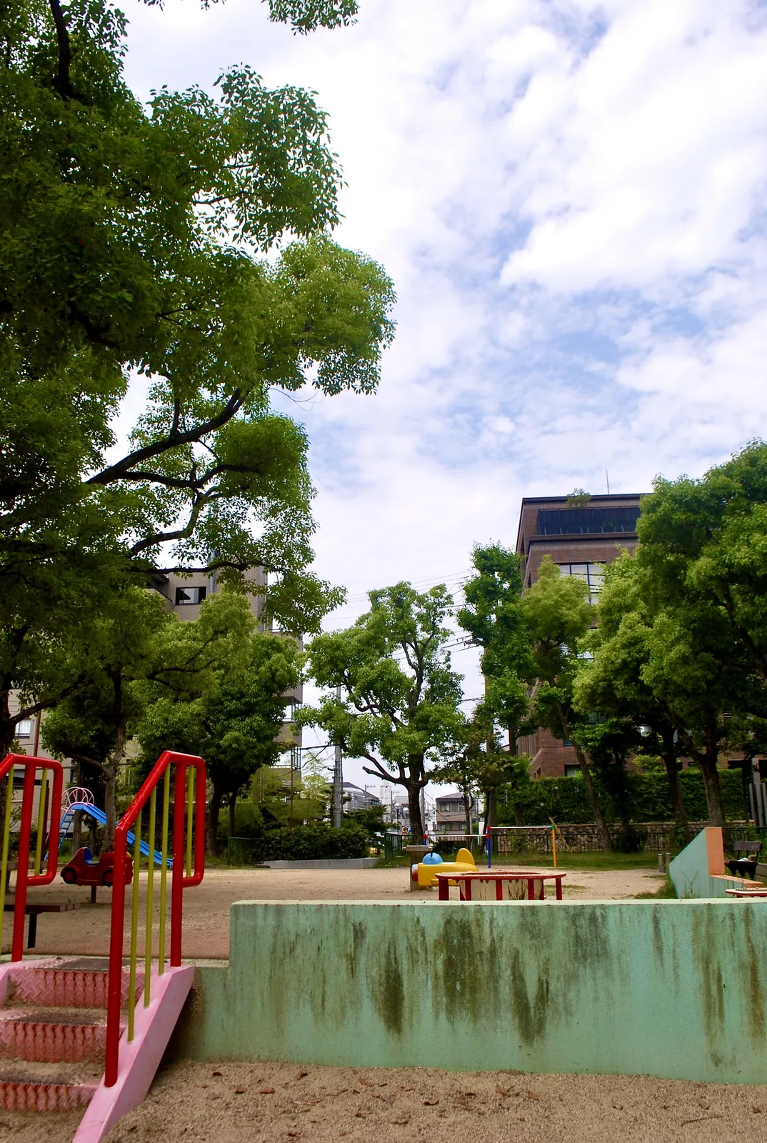 大きな木々に囲まれ、遊具の並ぶ公園
