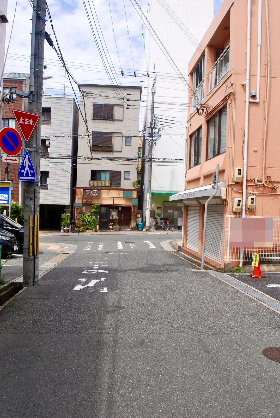 シャッターの店とピンクの建物が並ぶ、静かな交差点