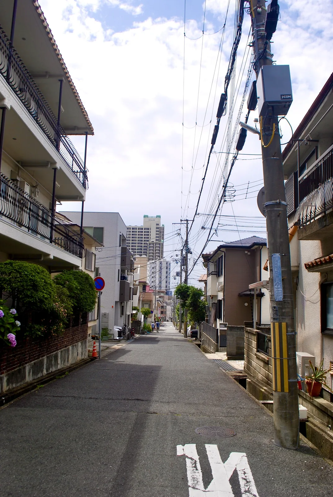 電柱と家々が並び、奥のマンションへまっすぐ続く通り