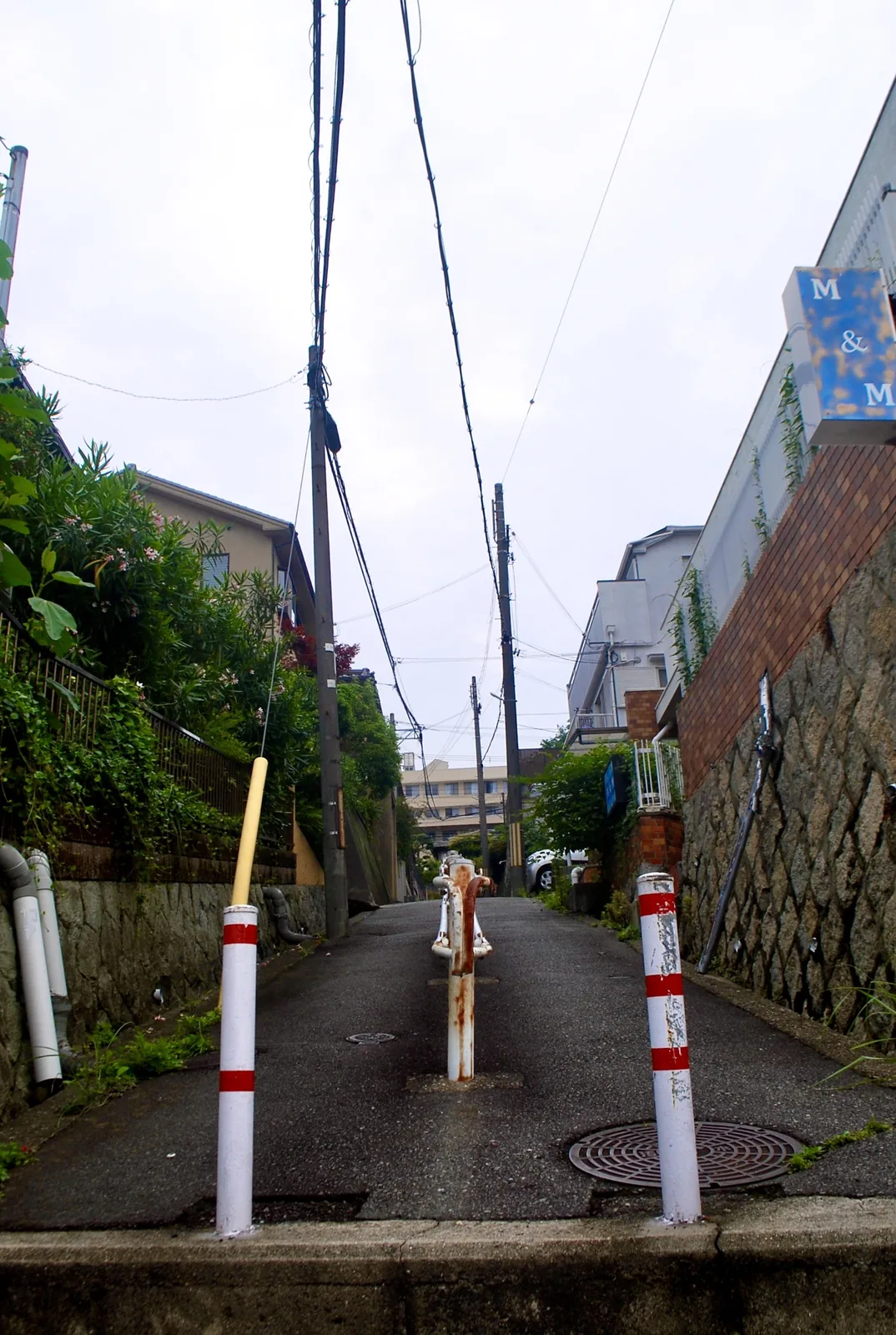 紅白の車止めが立ち、石垣とレンガの壁のあいだを上る坂道