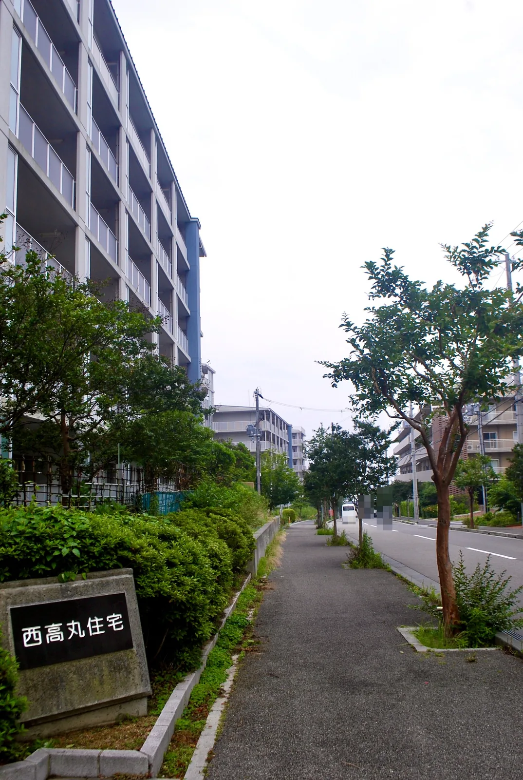「西高丸住宅」の銘板と、団地に沿って続く並木の歩道