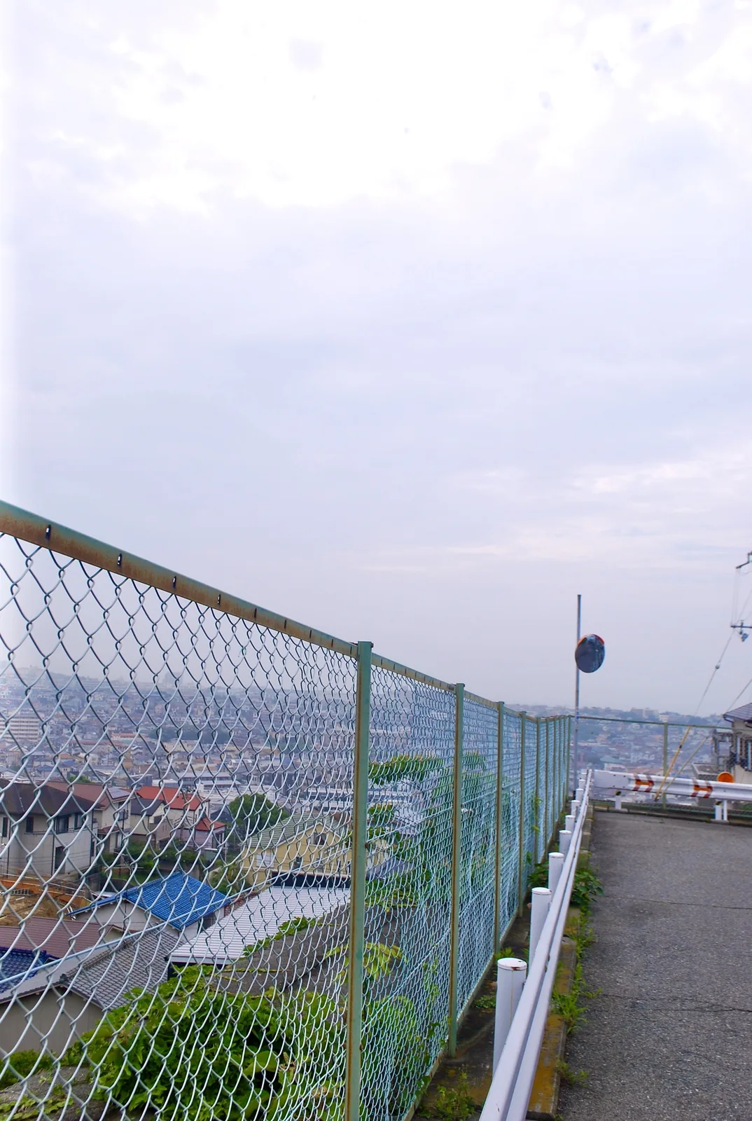 金網のフェンス越しに、坂の下に広がる家並みを見下ろす風景