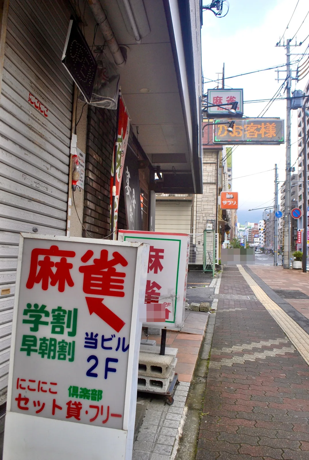赤い矢印の「麻雀」の立て看板が並ぶ、大通り沿いの歩道
