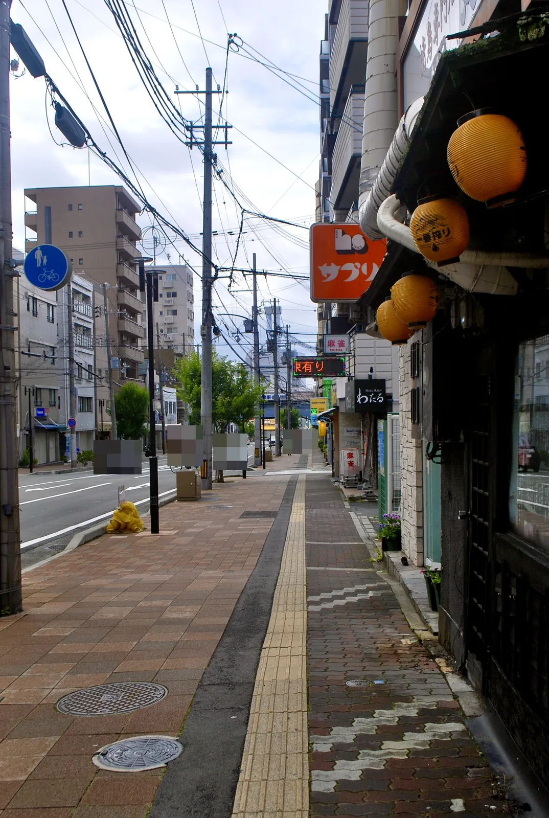 オレンジの提灯や看板が並ぶ店先と、大通り沿いの歩道
