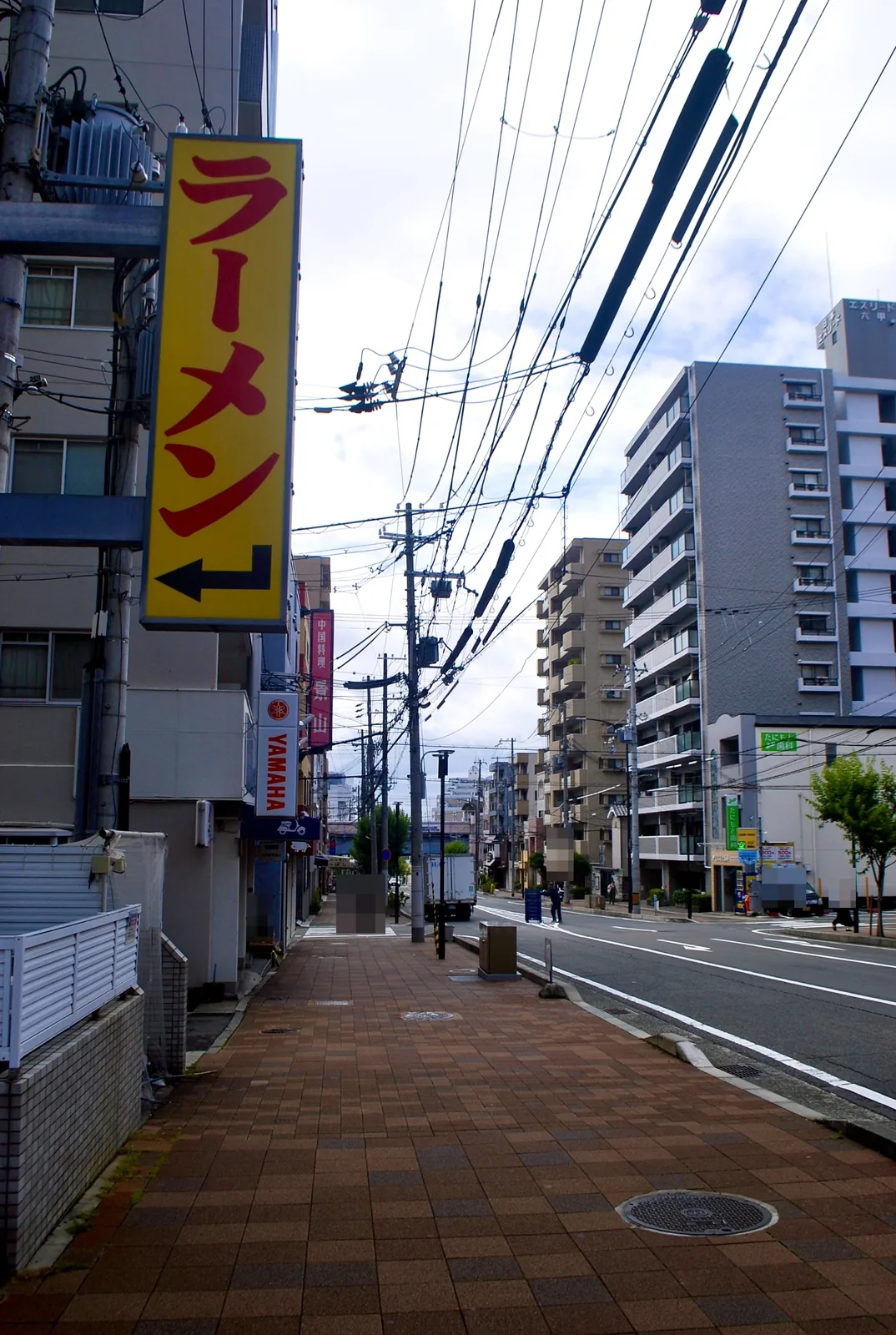 黄色い「ラーメン」の看板が目立つ、大通り沿いの歩道